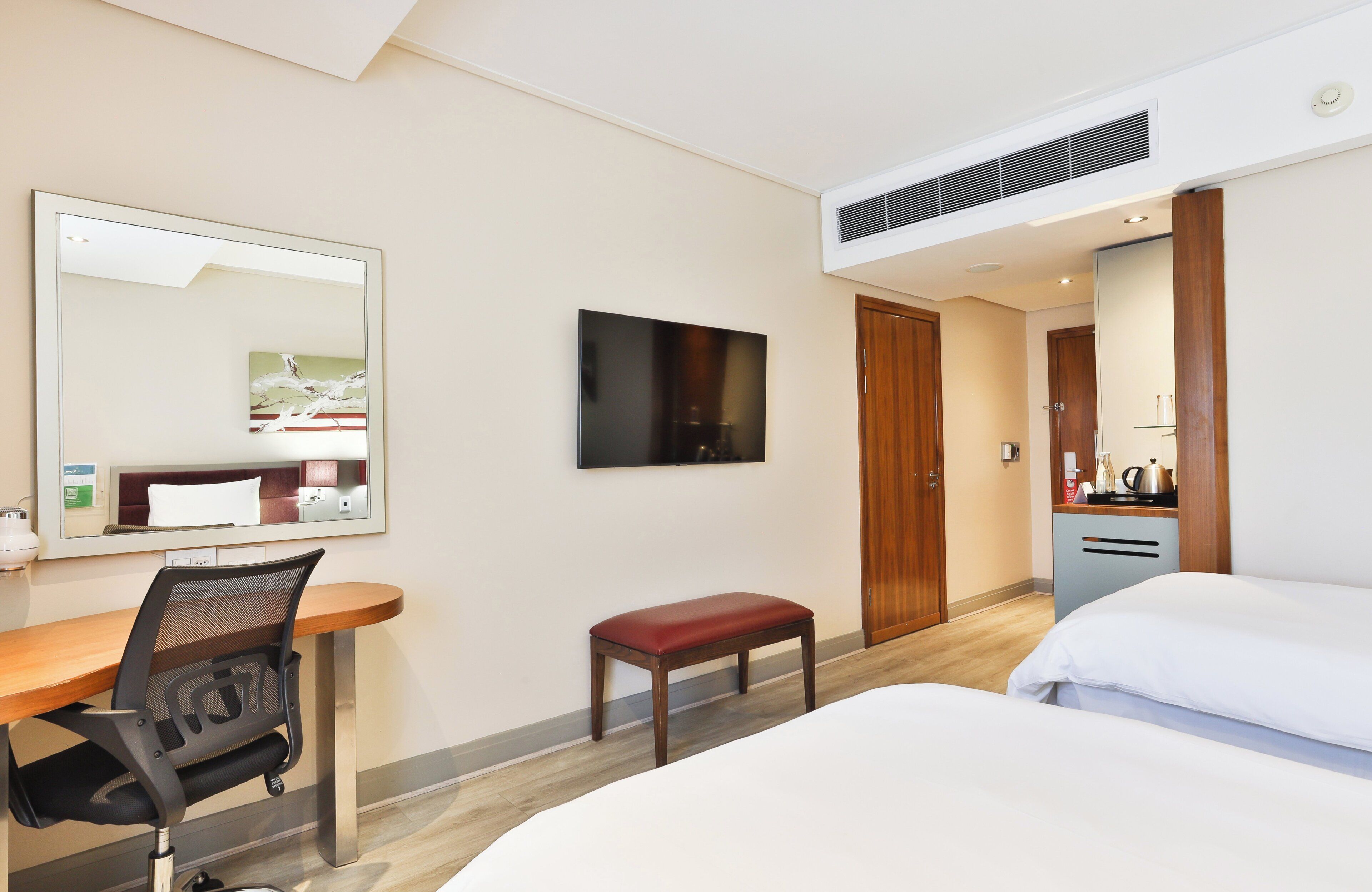 Habitación de hotel con cama, escritorio con silla, televisor, espejo y una zona de kitchenette.