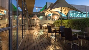 An outdoor patio area with wooden flooring, tables, chairs, and large umbrellas providing shade. - Holiday Inn Johannesburg - Rosebank by IHG (Johannesburg)