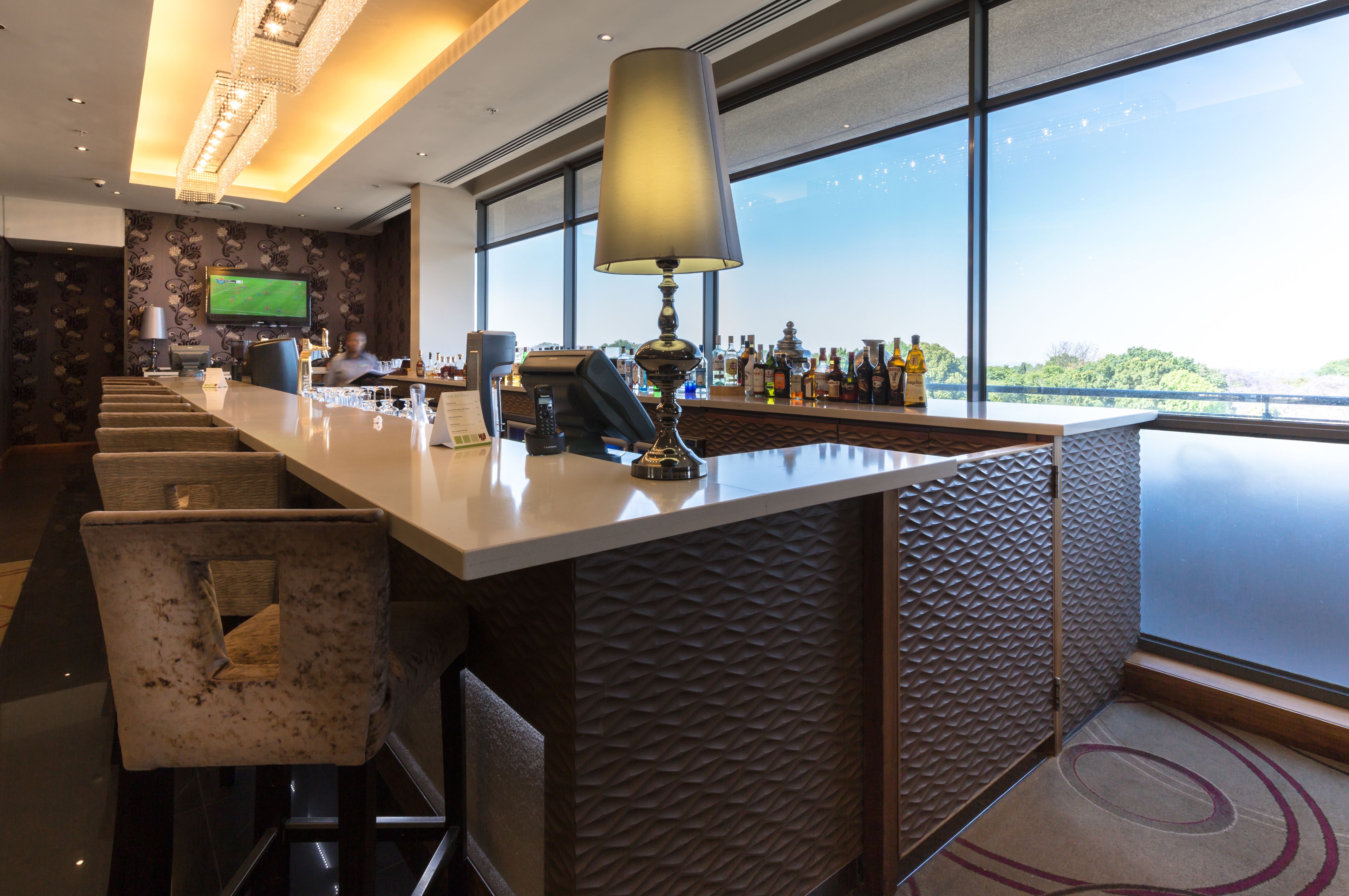 Zona de bar con una barra alargada, taburetes, una pantalla de televisión y vistas al exterior a través de amplios ventanales.
