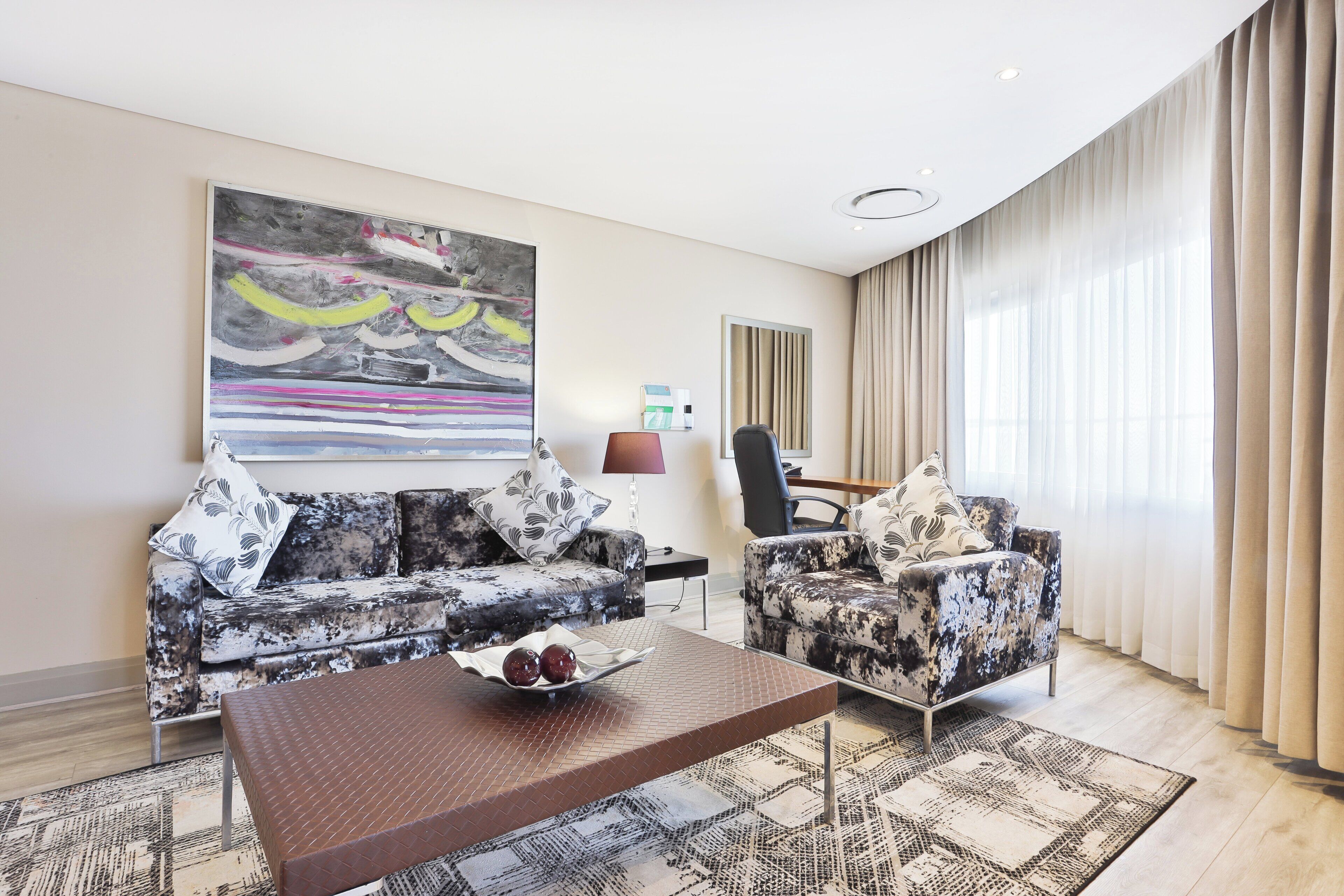 A modern living room with a sofa, armchair, coffee table, and abstract art.
