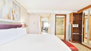 A hotel room with a large bed, a wooden wardrobe, a bench, and a view into the bathroom.