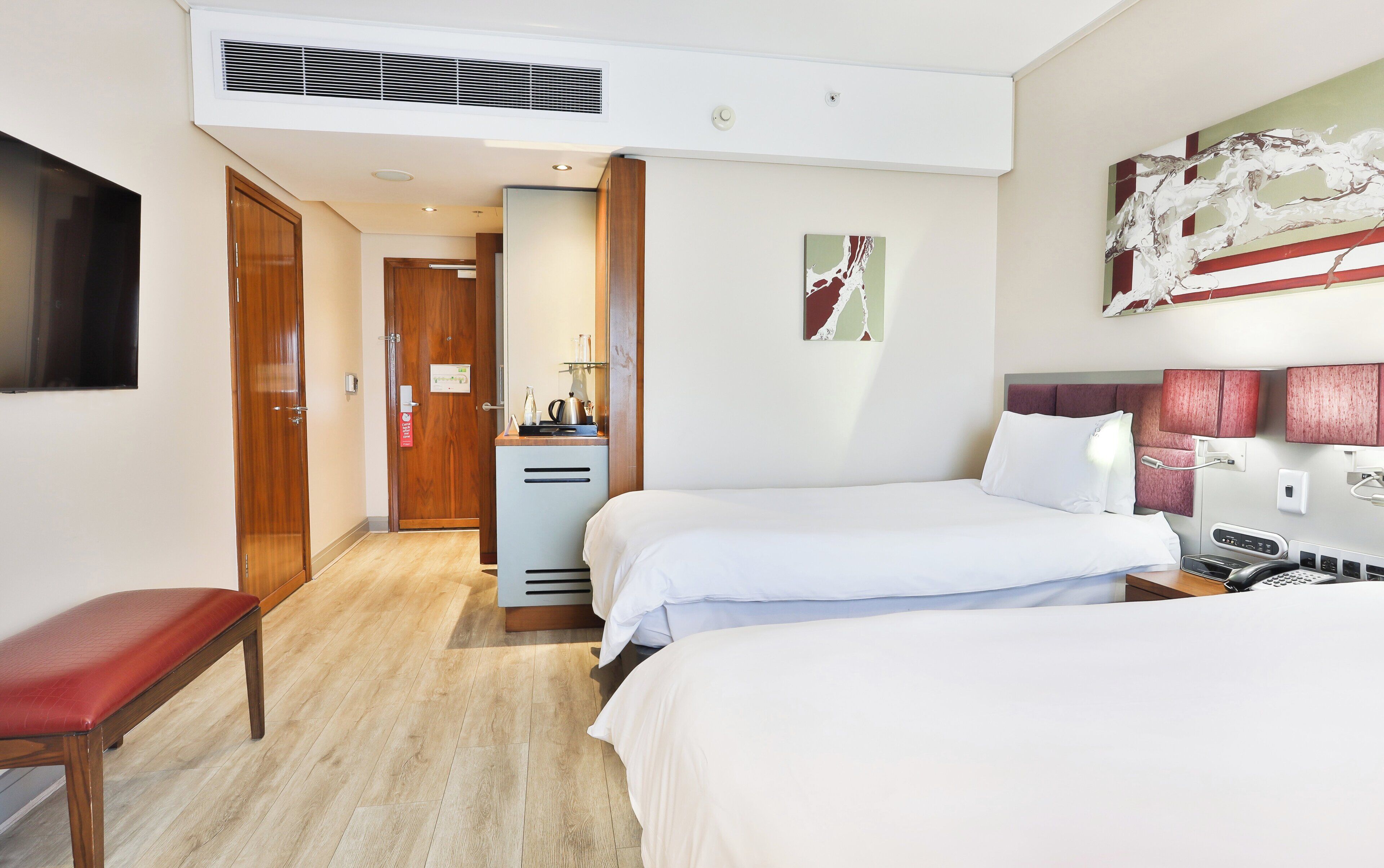 Een hotelkamer met twee bedden, een bureau, een stoel, een televisie en een schilderij aan de muur.