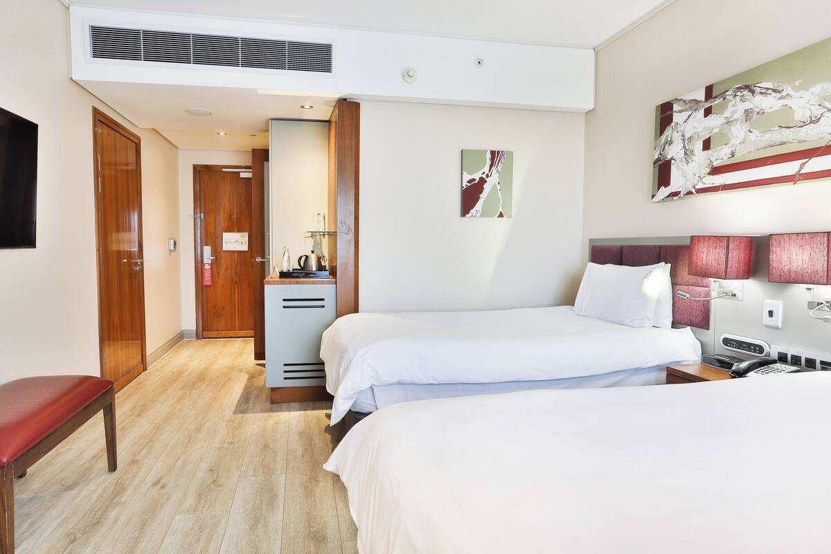 Ein Hotelzimmer mit zwei Betten, einem Schreibtisch, einem Stuhl, einem Fernseher und einem Bild an der Wand.