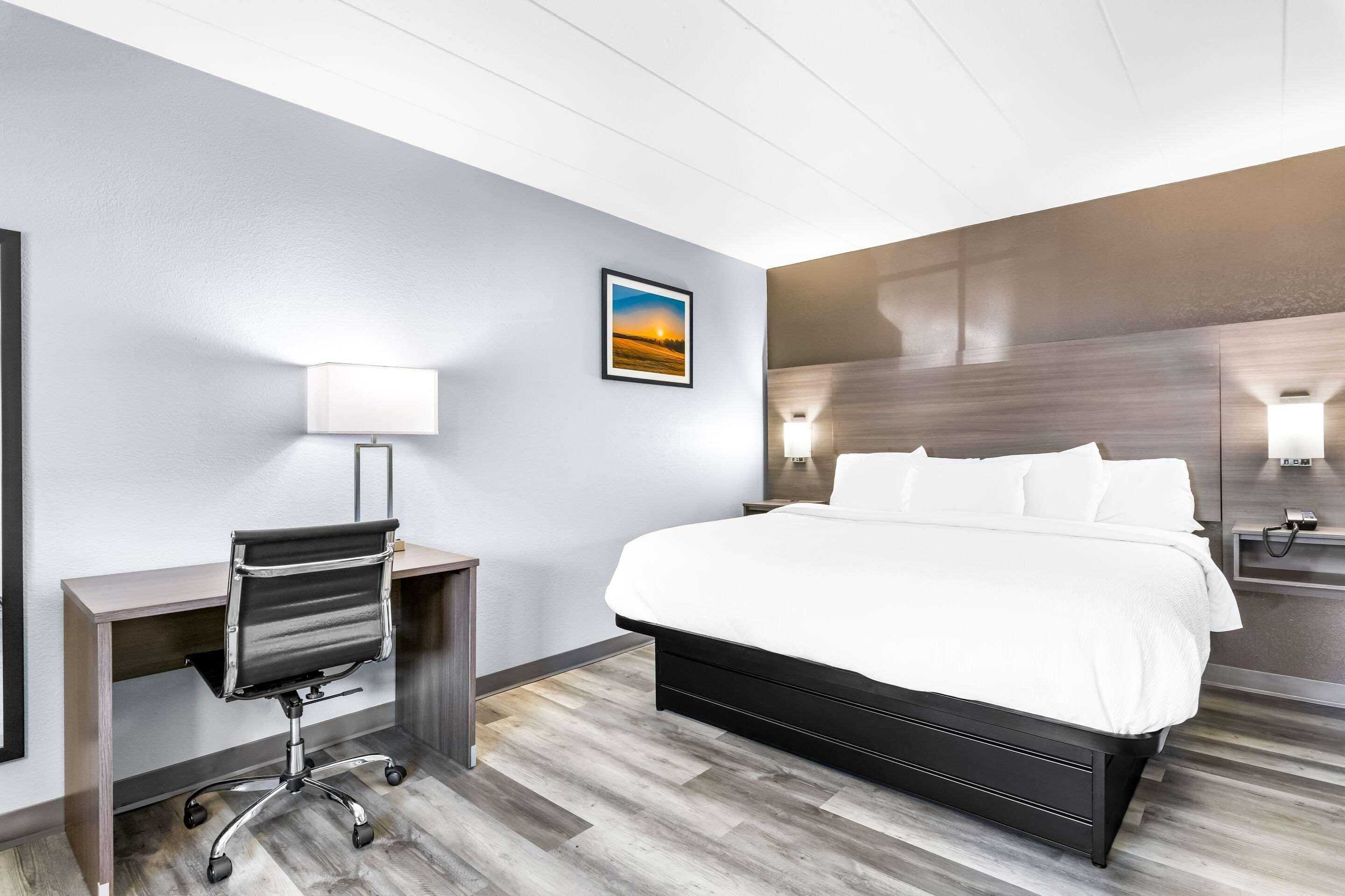 Ett hotellrum med en säng, ett skrivbord, en stol och en tavla på väggen.