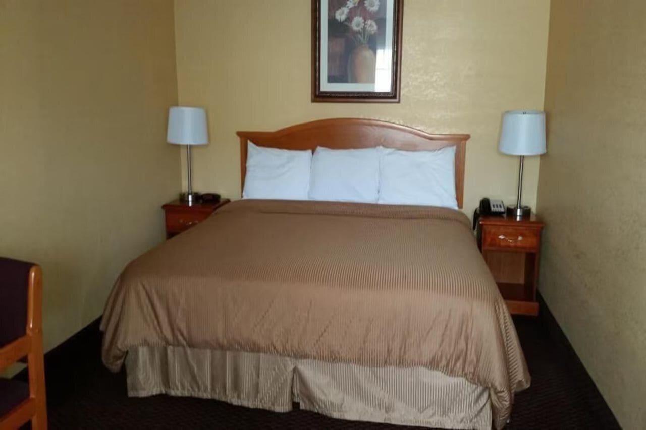 A hotel room with a large bed, two bedside tables with lamps, a chair, and a framed picture on the wall.