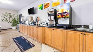 Een moderne keuken met houten kastjes, een koffieapparaat, een sapdispenser en een flatscreen televisie aan de muur.
