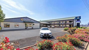Un bâtiment à deux étages, avec une enseigne « Quality Inn », un parking où se trouve une voiture blanche, et des parterres de fleurs aménagés devant.