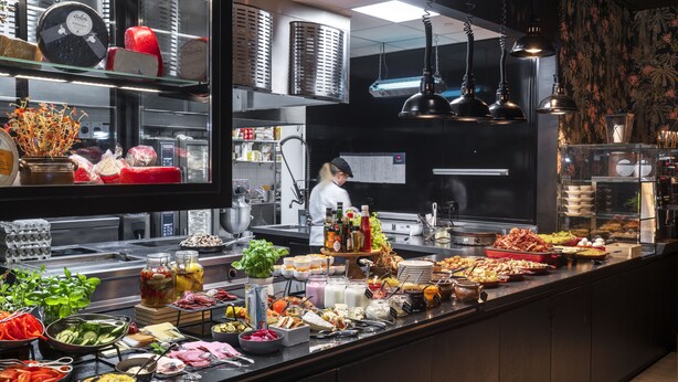 A buffet with various food items and condiments, a chef in the background, and kitchen equipment. - Thon Hotel Alta (Alta)