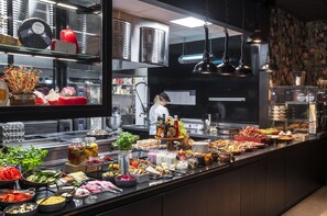 A buffet with various food items and condiments, a chef in the background, and kitchen equipment. - Thon Hotel Alta (Alta)