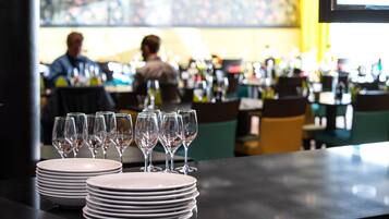 A bar area with stacked plates and wine glasses, a bar counter, and a seating area with chairs.