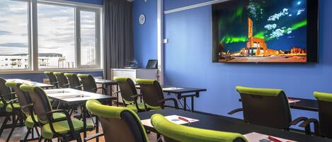 Un salón de conferencias con mesas y sillas, un ventanal grande y una pantalla en la pared que muestra la aurora boreal.