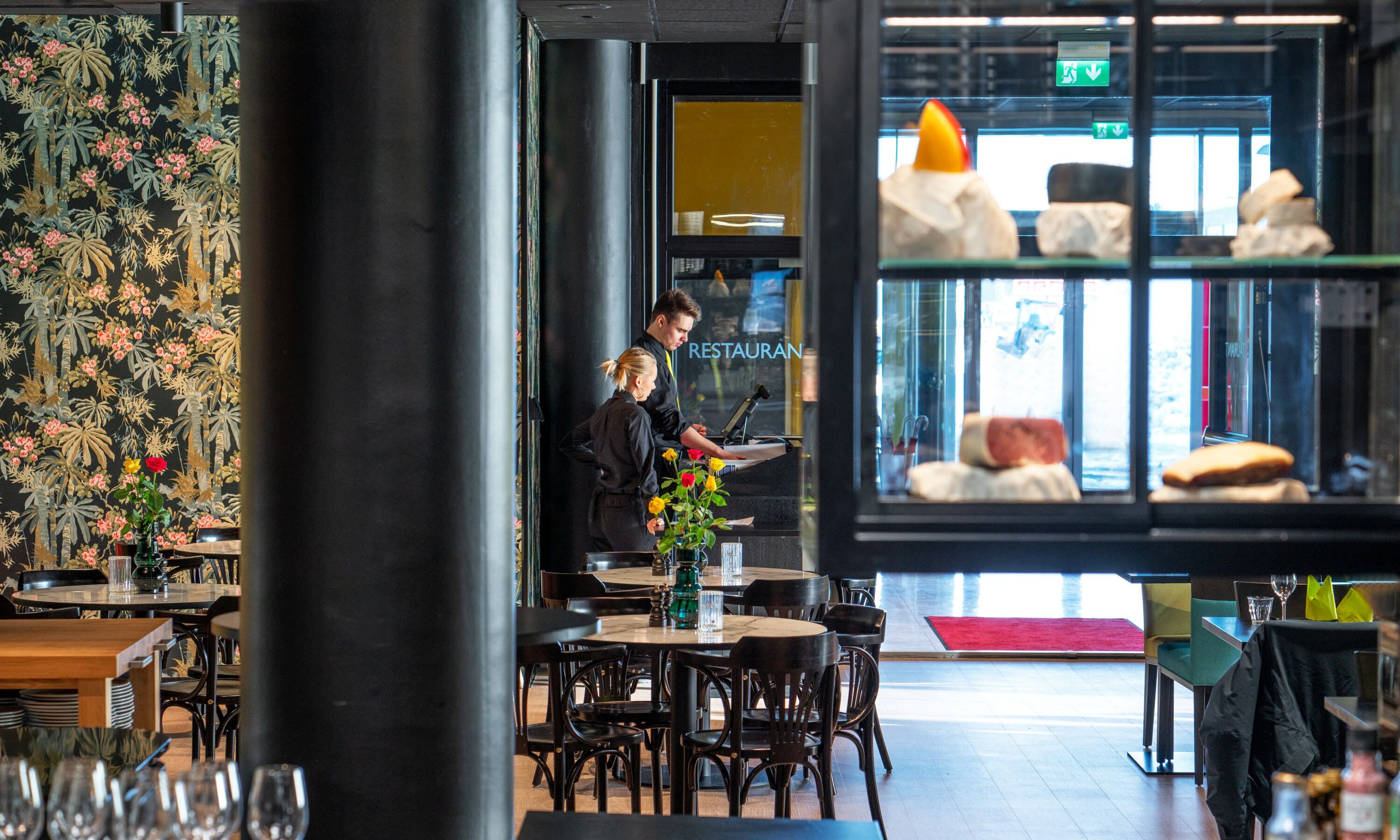 En restauranginteriör med bord, stolar och utsikt över gatan genom ett fönster.