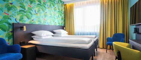 A hotel room with a bed, two chairs, a desk, and a large window with curtains.