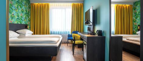 A hotel room with two beds, a desk, a chair, a mirror, and a window with yellow curtains.
