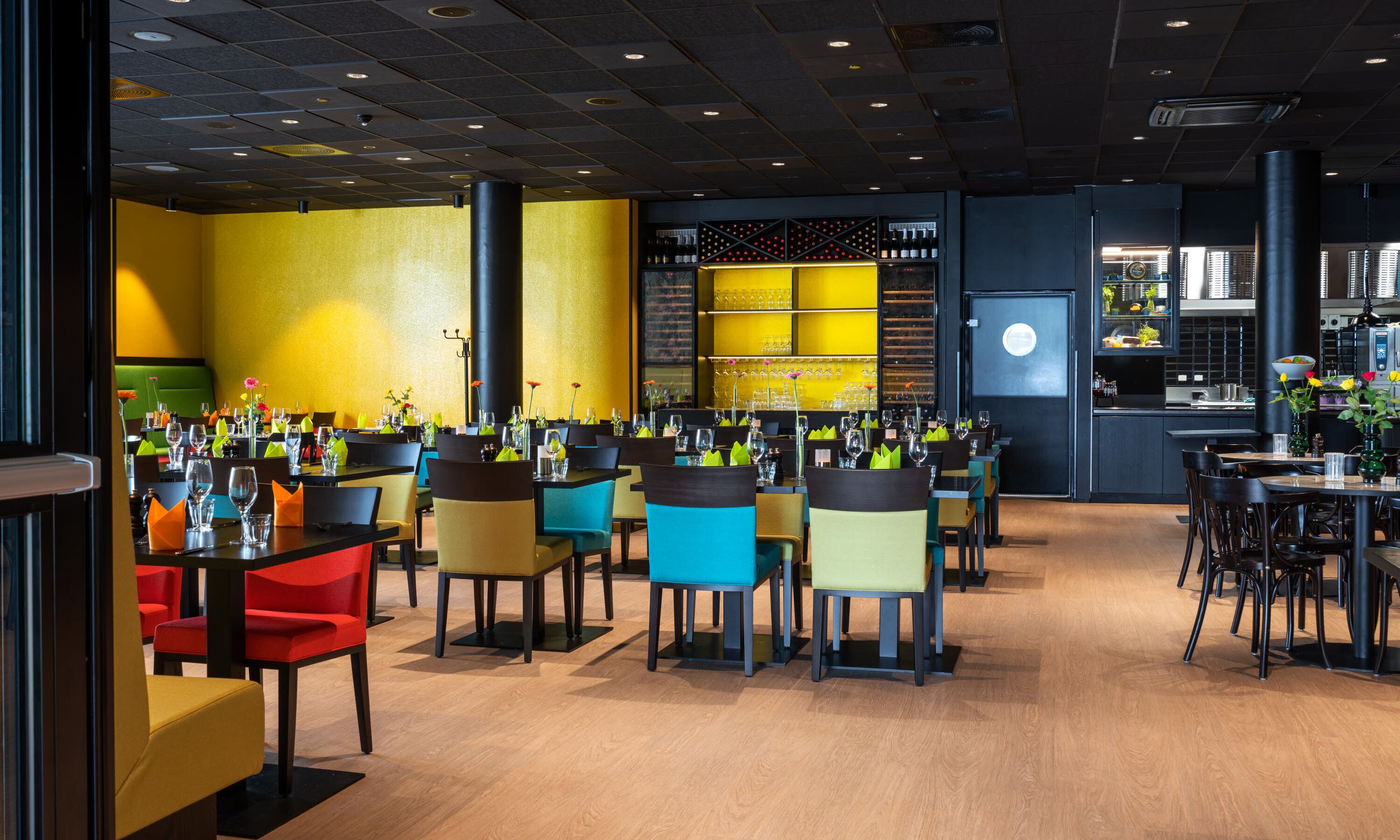 L’intérieur d’un restaurant moderne, avec plusieurs tables et chaises, un bar et une cuisine visible au fond.