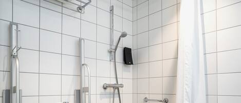 A small, modern bathroom with a white toilet, a handheld showerhead, and a grab bar.