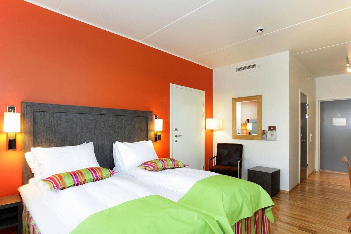 A hotel room with two beds, a chair, a desk, and a mirror on the wall.