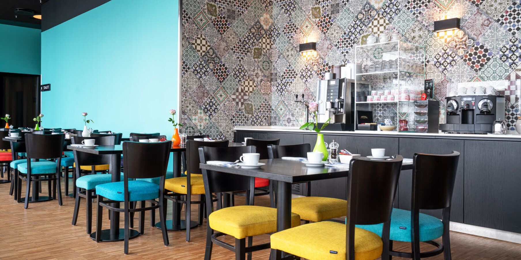 A restaurant with multiple tables and chairs, a coffee bar, and a patterned wall.