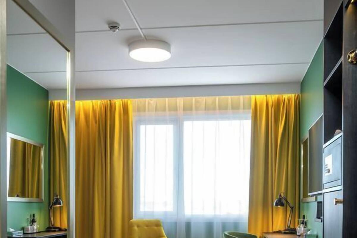 Una habitación de hotel con cama, escritorio, silla, espejo y ventana con cortinas.