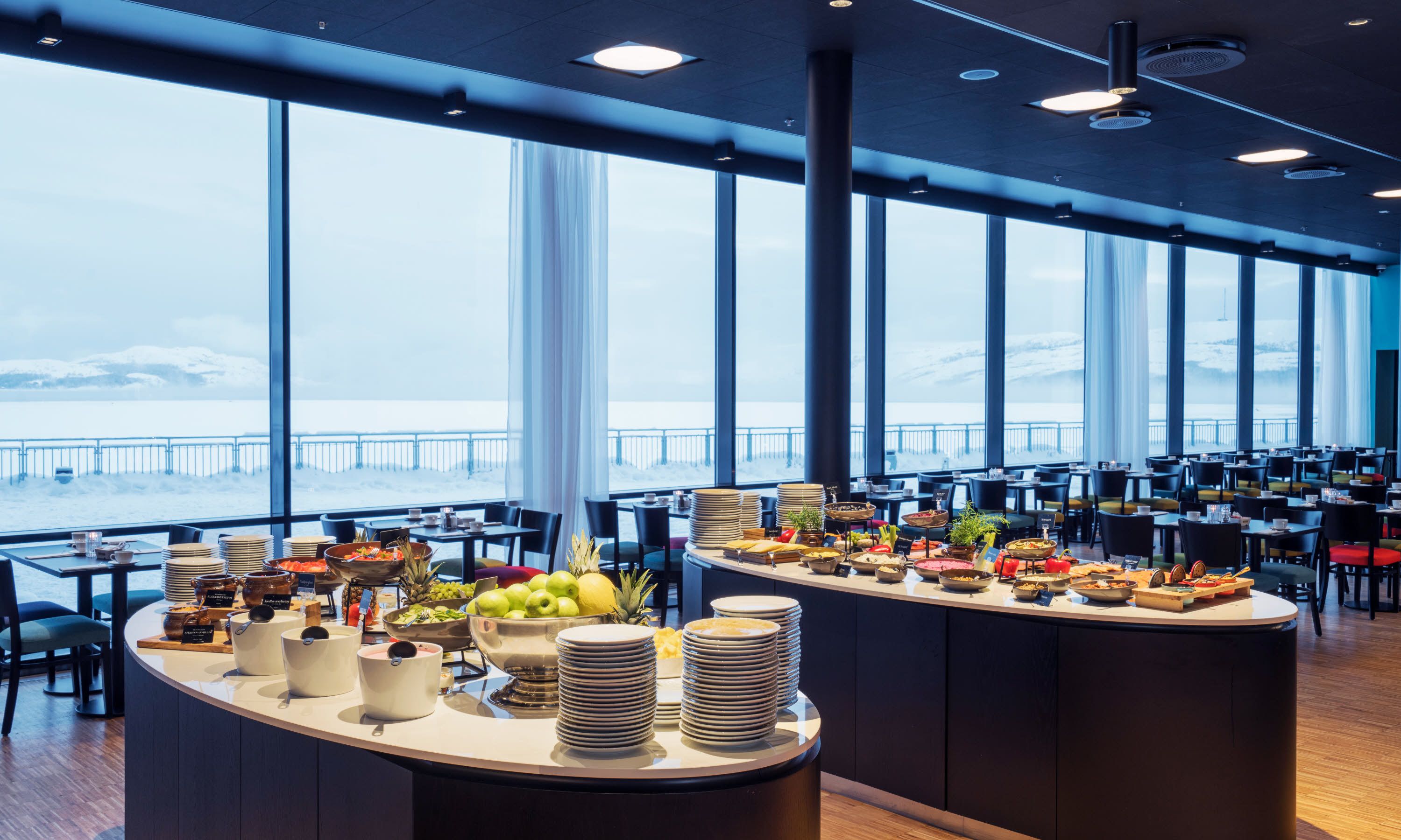 A buffet setup with various food items and a view of the sea through large windows.