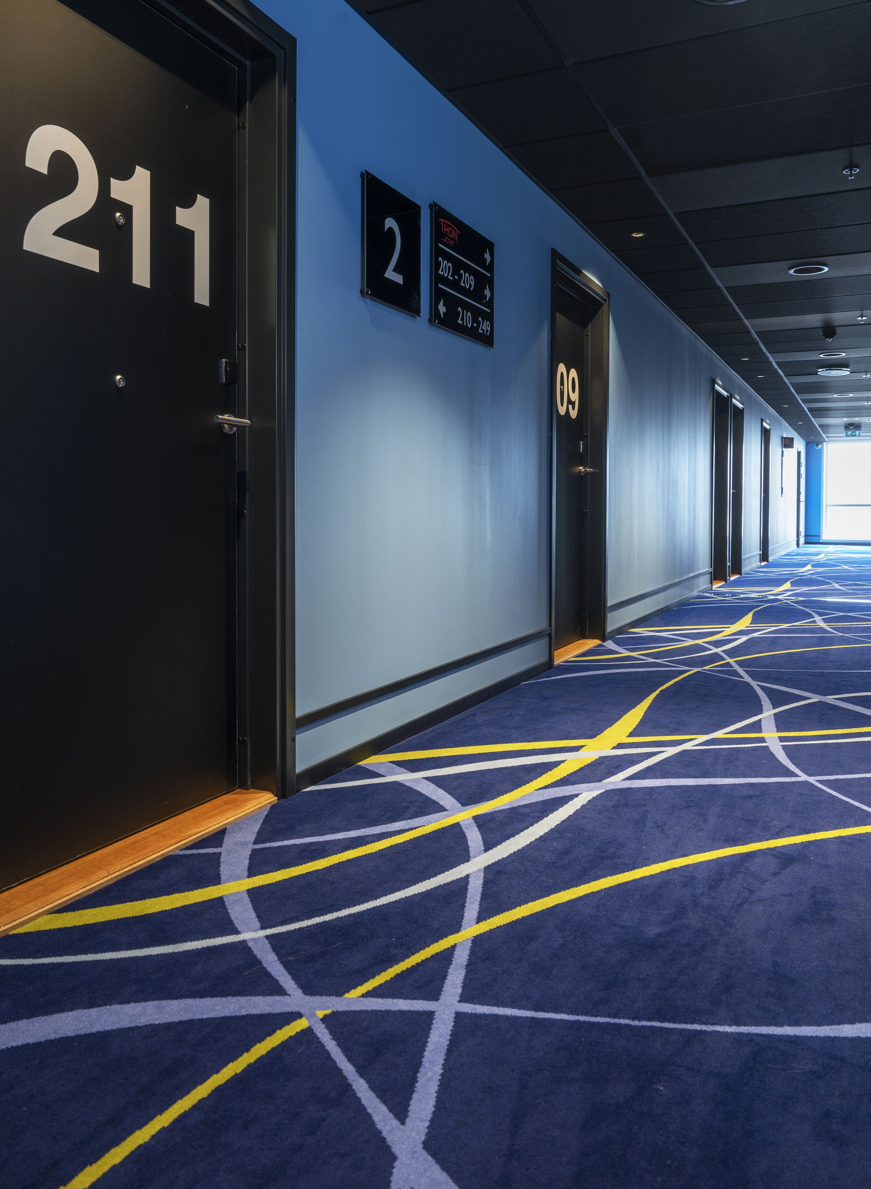 Un pasillo de hotel con puertas numeradas 211, 2 y 09, y señales indicativas para las habitaciones 202 a 209 y 210 a 249.