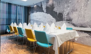 Un comedor con una mesa larga dispuesta para una comida, rodeada de sillas con tapicería azul verdoso y amarilla.