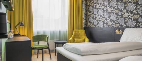 Una habitación de hotel con una cama, un escritorio con lámpara, una silla y una mesita.