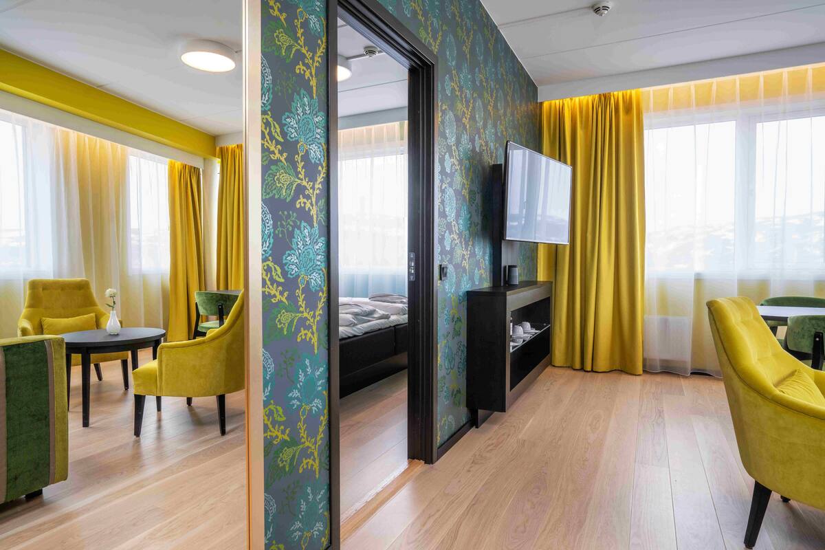 Quarto de hotel com cama, televisão, escrivaninha e cadeiras.
