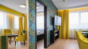Hotellihuone, jossa on sänky, televisio, työpöytä ja tuoleja.