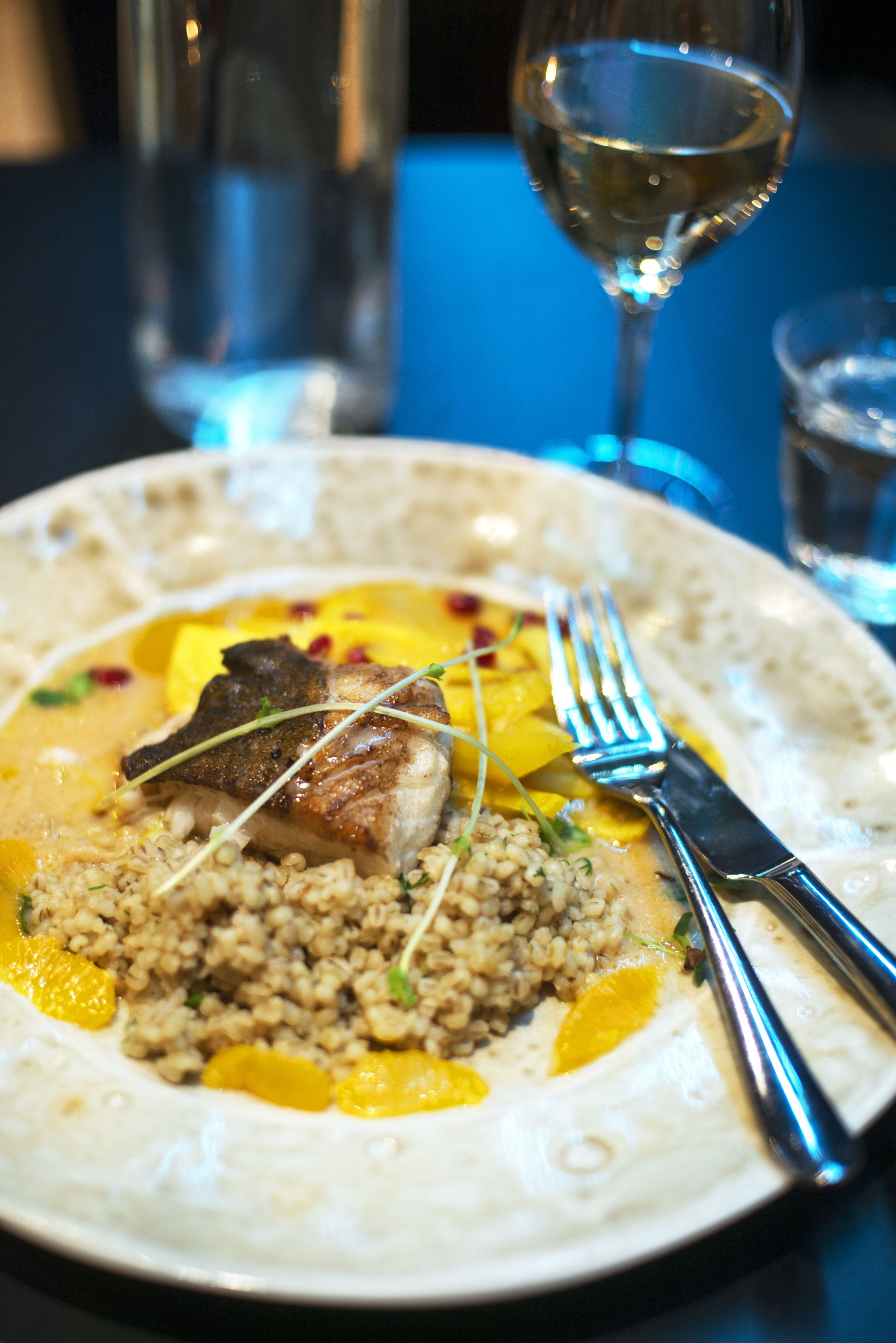 A plate of food with a fork and knife, a glass of white wine, and a bottle in the background.