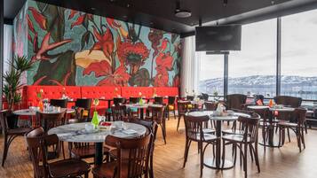 A restaurant with round tables and chairs, a red cushioned bench, and a large mural of flowers on the wall.