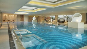 Un'ampia piscina coperta dal design moderno, con pavimento decorato e zona centrale con una grande scultura bianca.