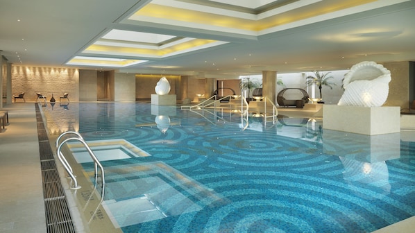 Una amplia piscina interior de diseño moderno, con suelo estampado y una zona de estar central con una gran escultura blanca.