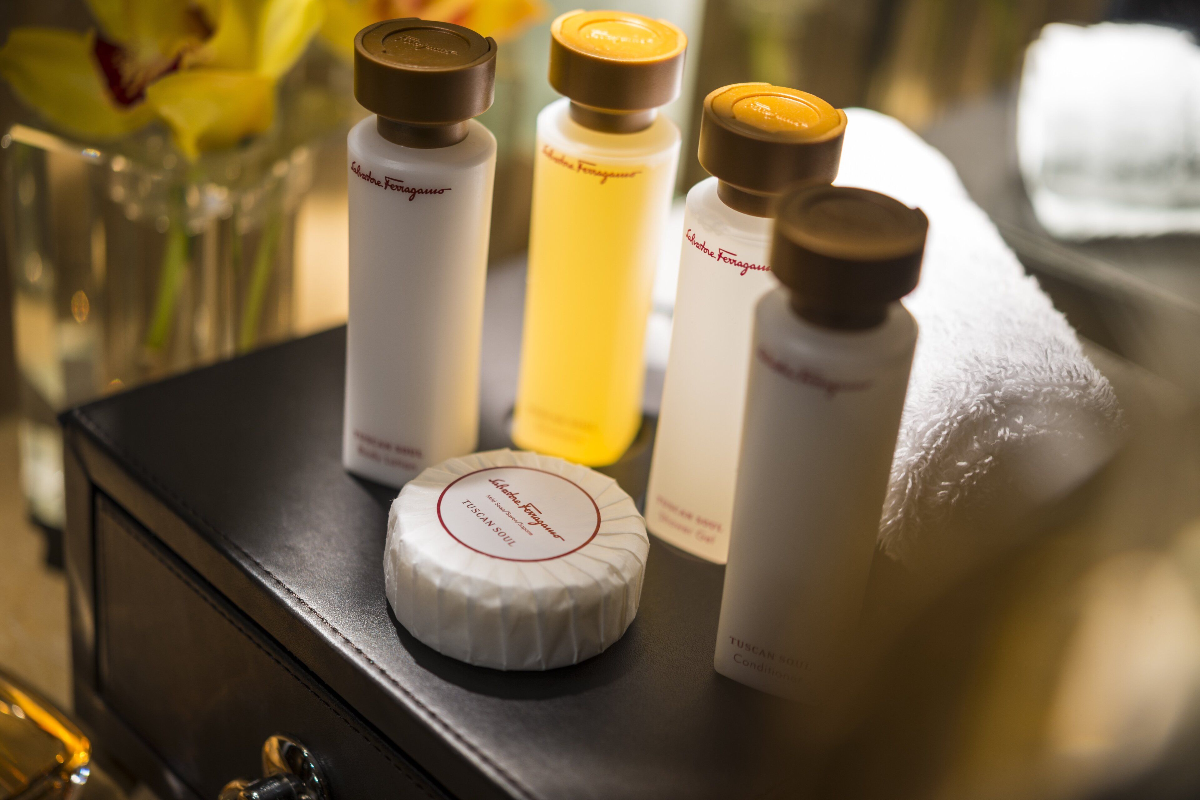 A selection of skincare products on a table, including a white round container labeled "Tuscany Soak" and three bottles with brown caps.