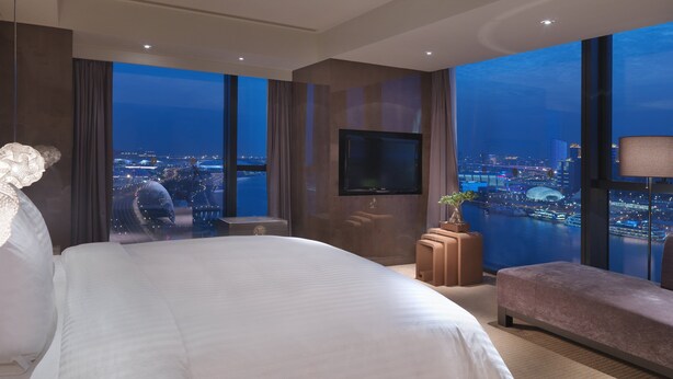 Camera d'albergo moderna con un letto grande, una televisione a schermo piatto, una panca e vista sulla città di notte.