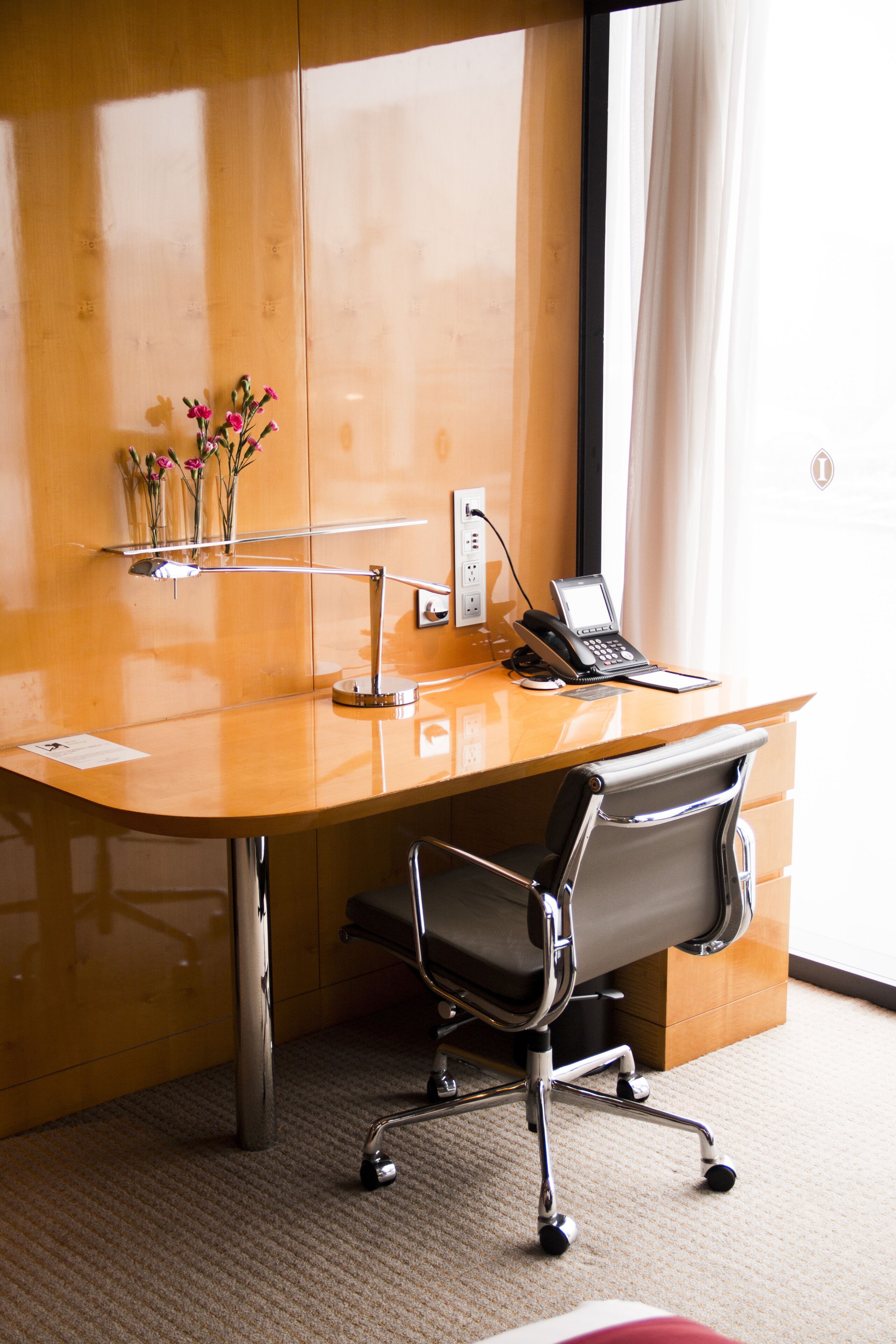 A wooden desk with a laptop, a telephone, and a vase with flowers.