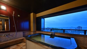 A modern bathroom with a glass-enclosed hot tub, a shower, and a view of the cityscape at dusk. - Biwako Hanakaido (Otsu)