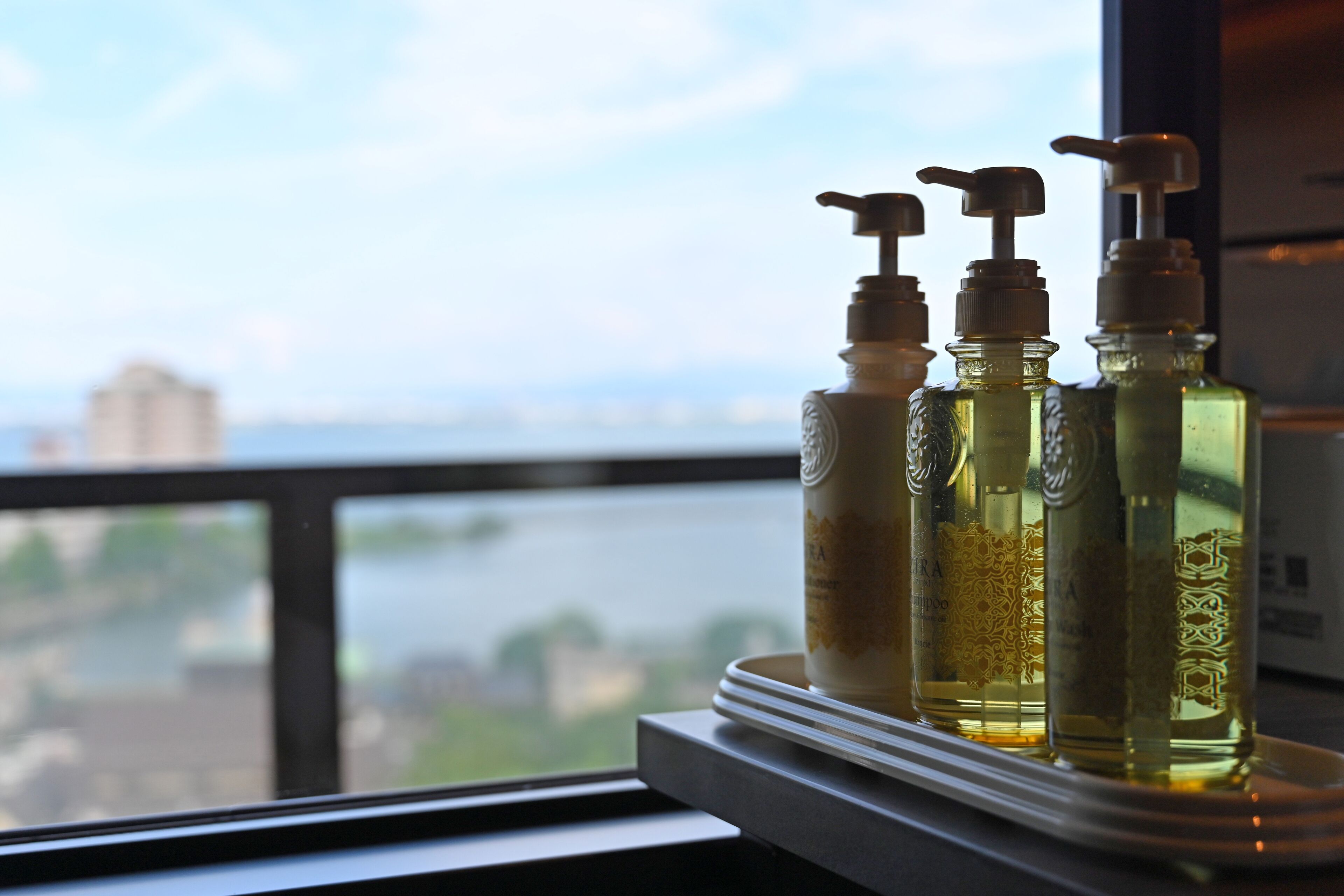 Three bottles of liquid on a tray by a window overlooking a river.