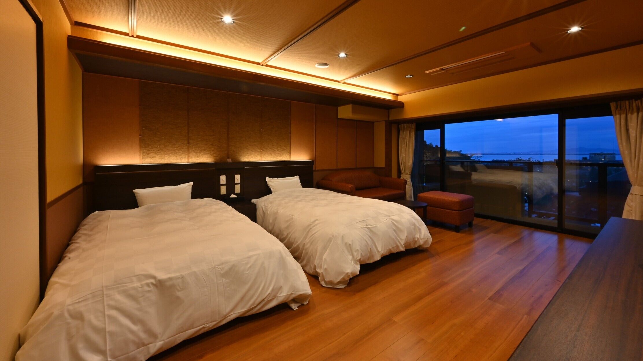 A hotel room with two beds, a sofa, a small table, and a balcony with a view.