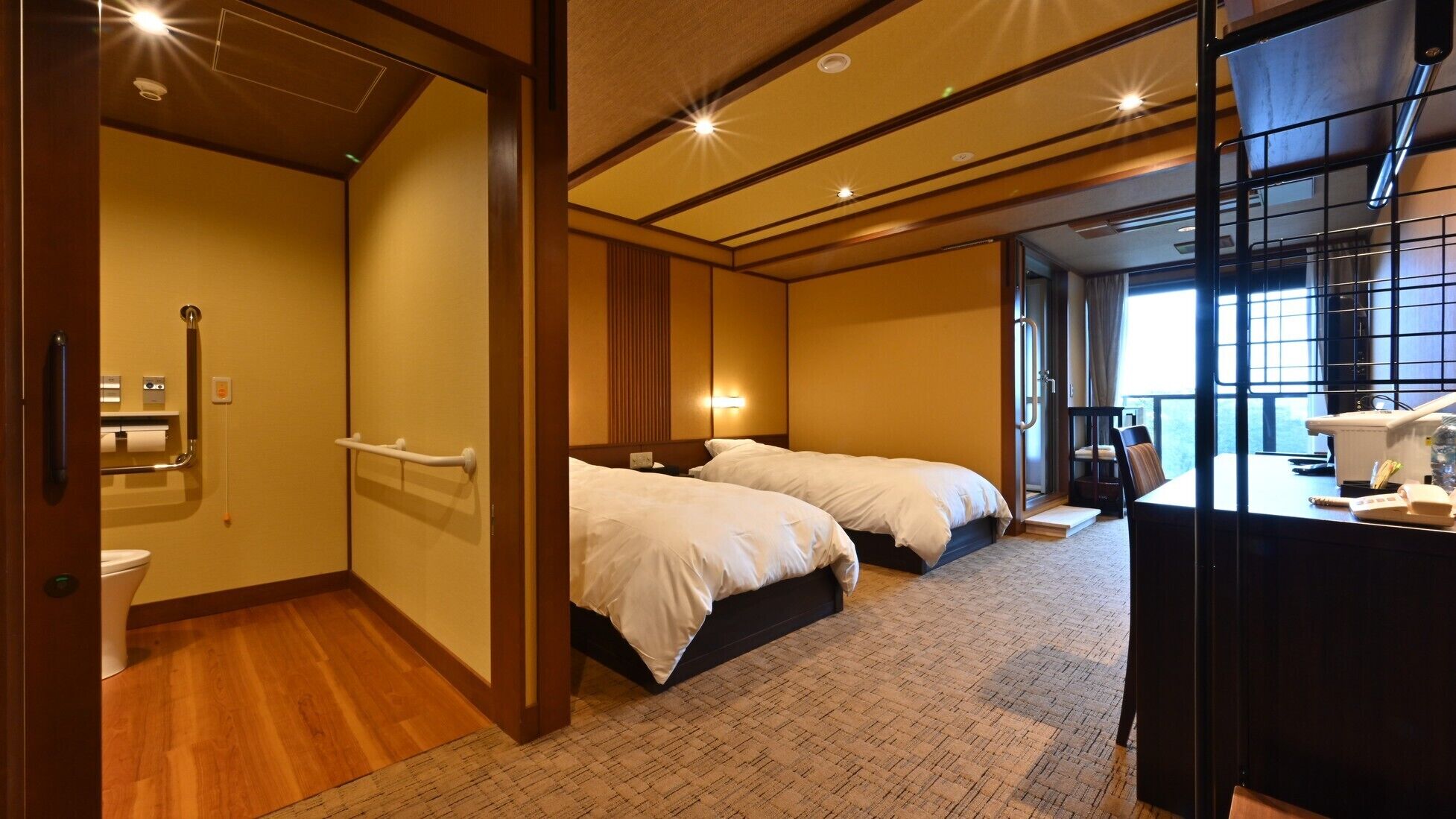 A hotel room with two beds, a desk with a computer, and a large window.