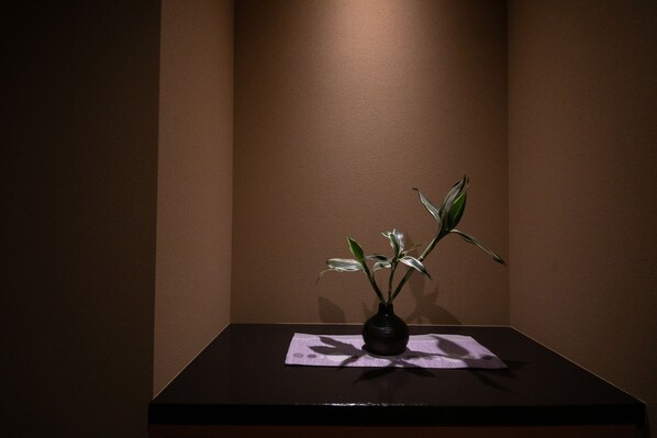 A dark wooden table with a vase containing a plant, set against a plain wall. - Biwako Hanakaido (Otsu)