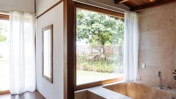 Enjoy a serene view of the garden from the large window, featuring a bathtub and a framed picture.