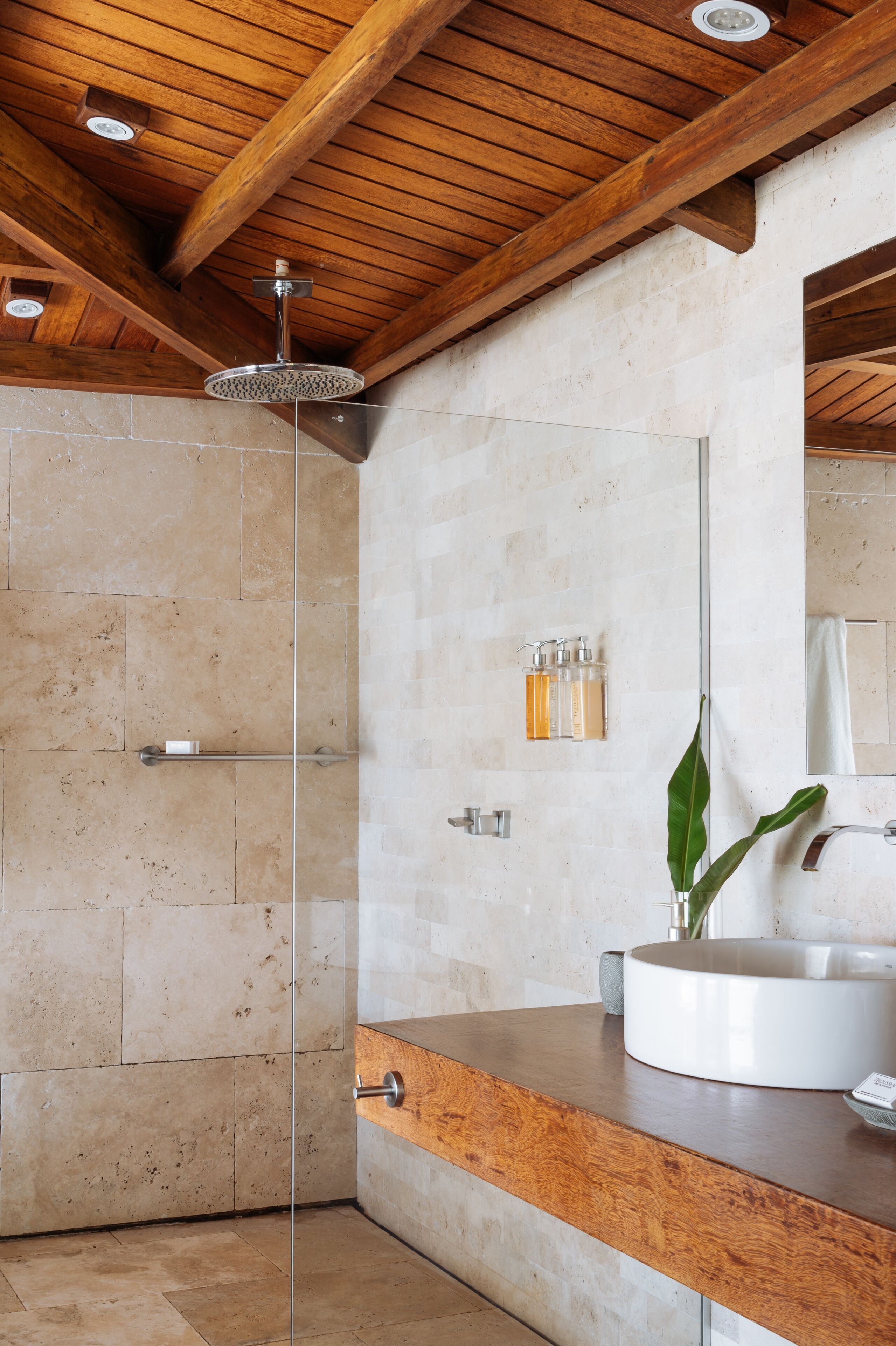 A modern bathroom with a glass-enclosed shower, a wooden ceiling, and a large mirror.