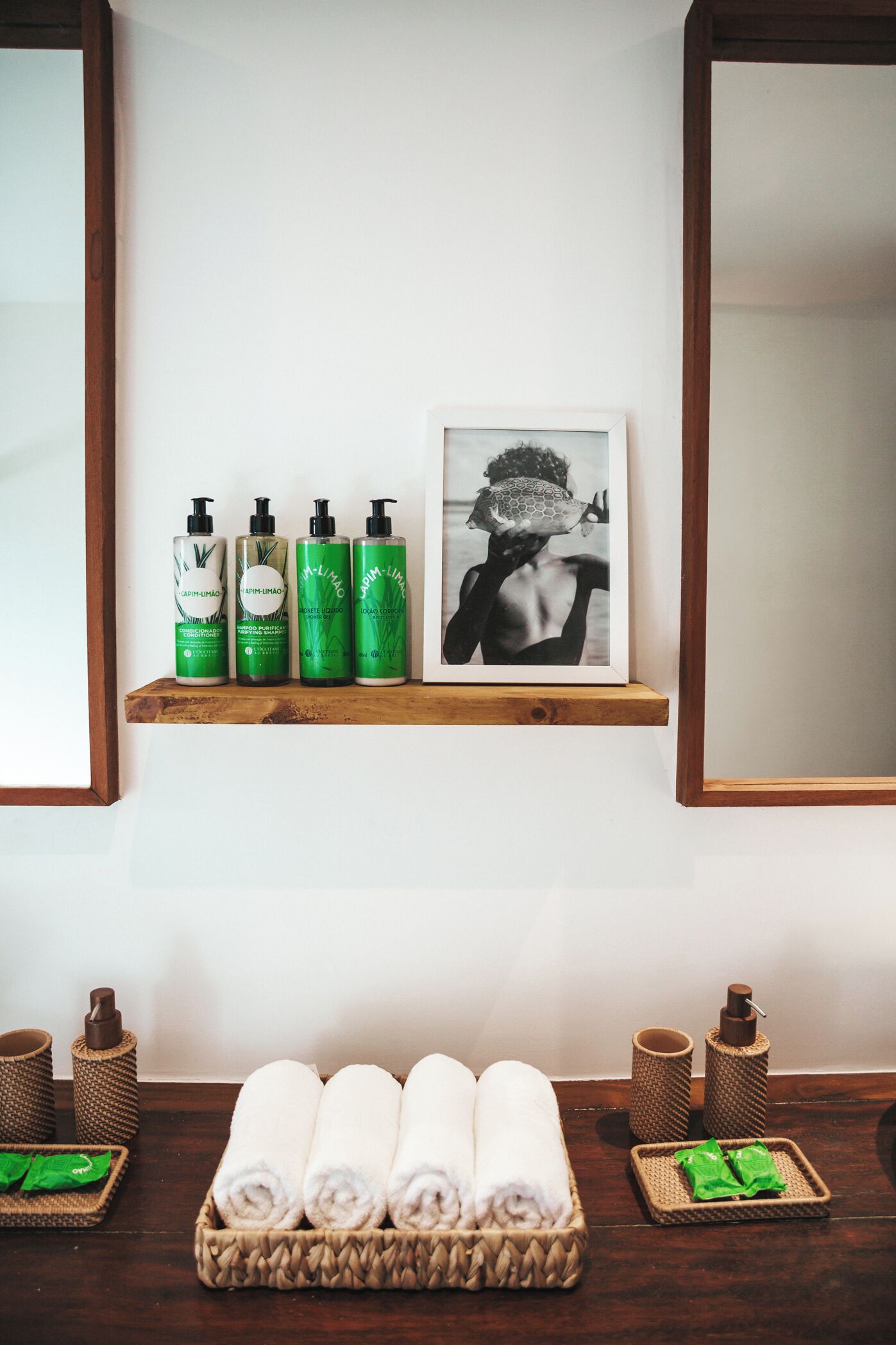 A shelf with four bottles of green body wash, a framed black and white photo, and a wooden tray with rolled towels.