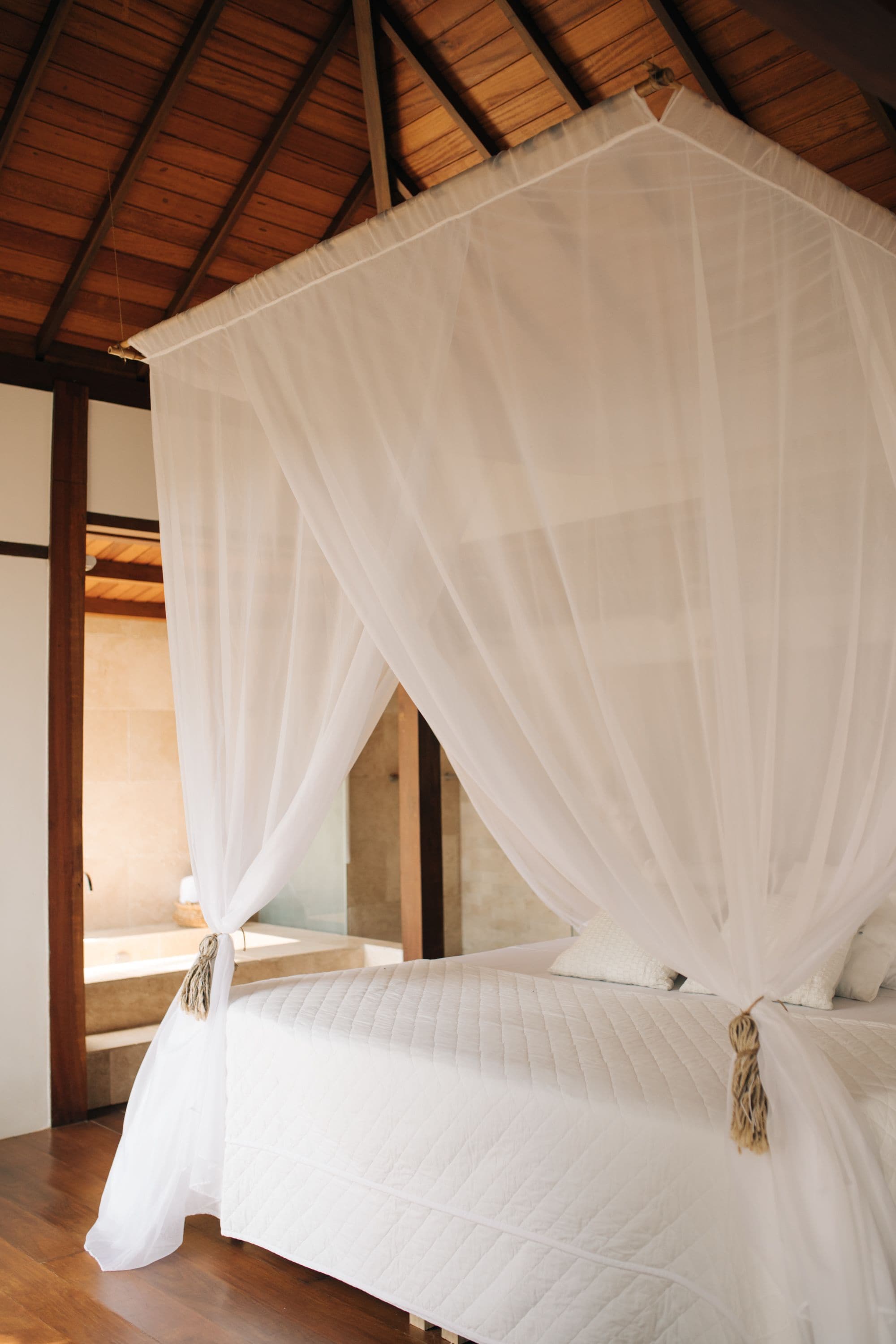 Quarto com cama sob um dossel, vigas de madeira no teto e vista para uma parede de pedra.