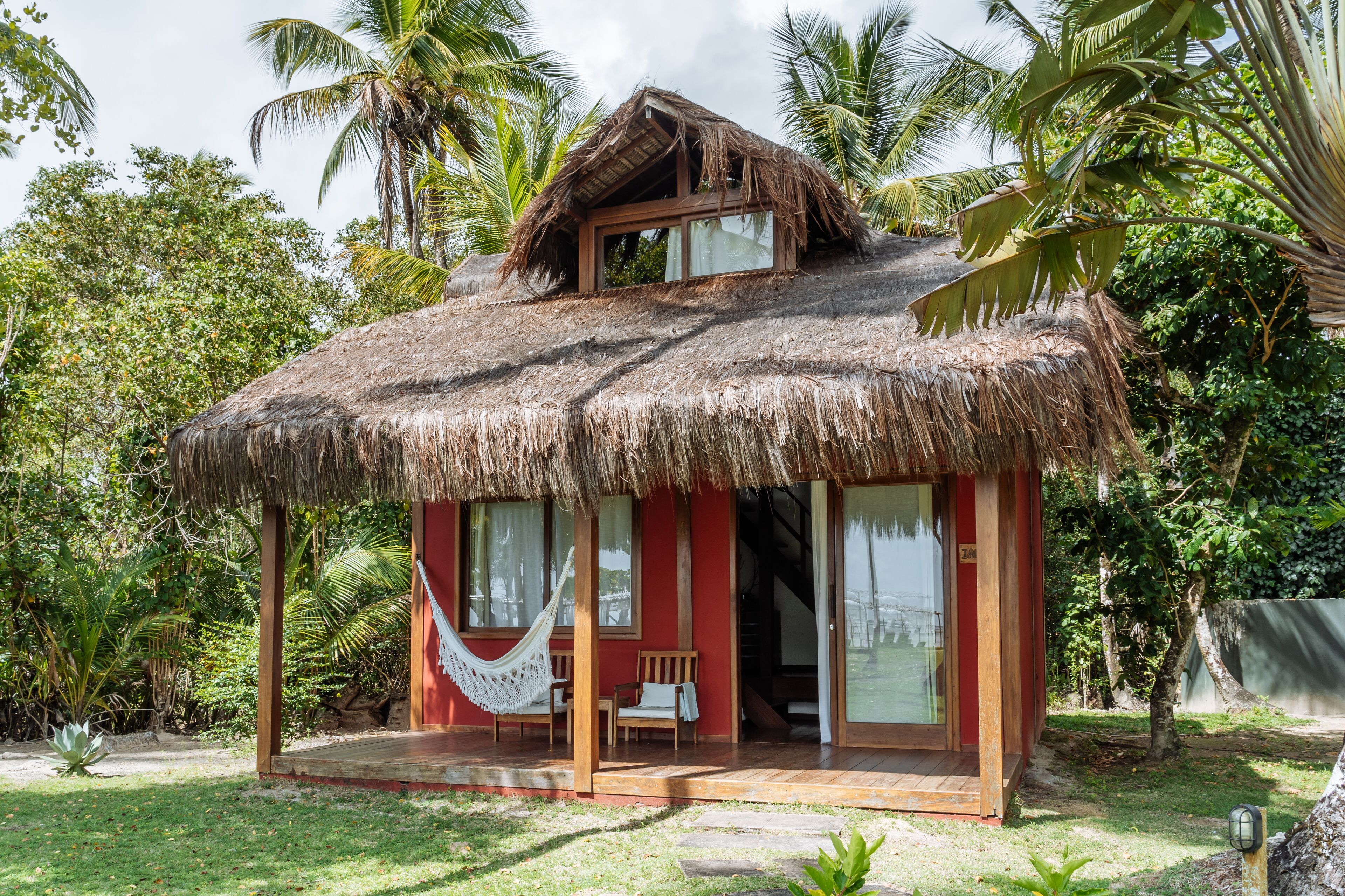 Un bungalow au toit de chaume, doté d’une terrasse en bois, d’un hamac et d’une porte-fenêtre coulissante.
