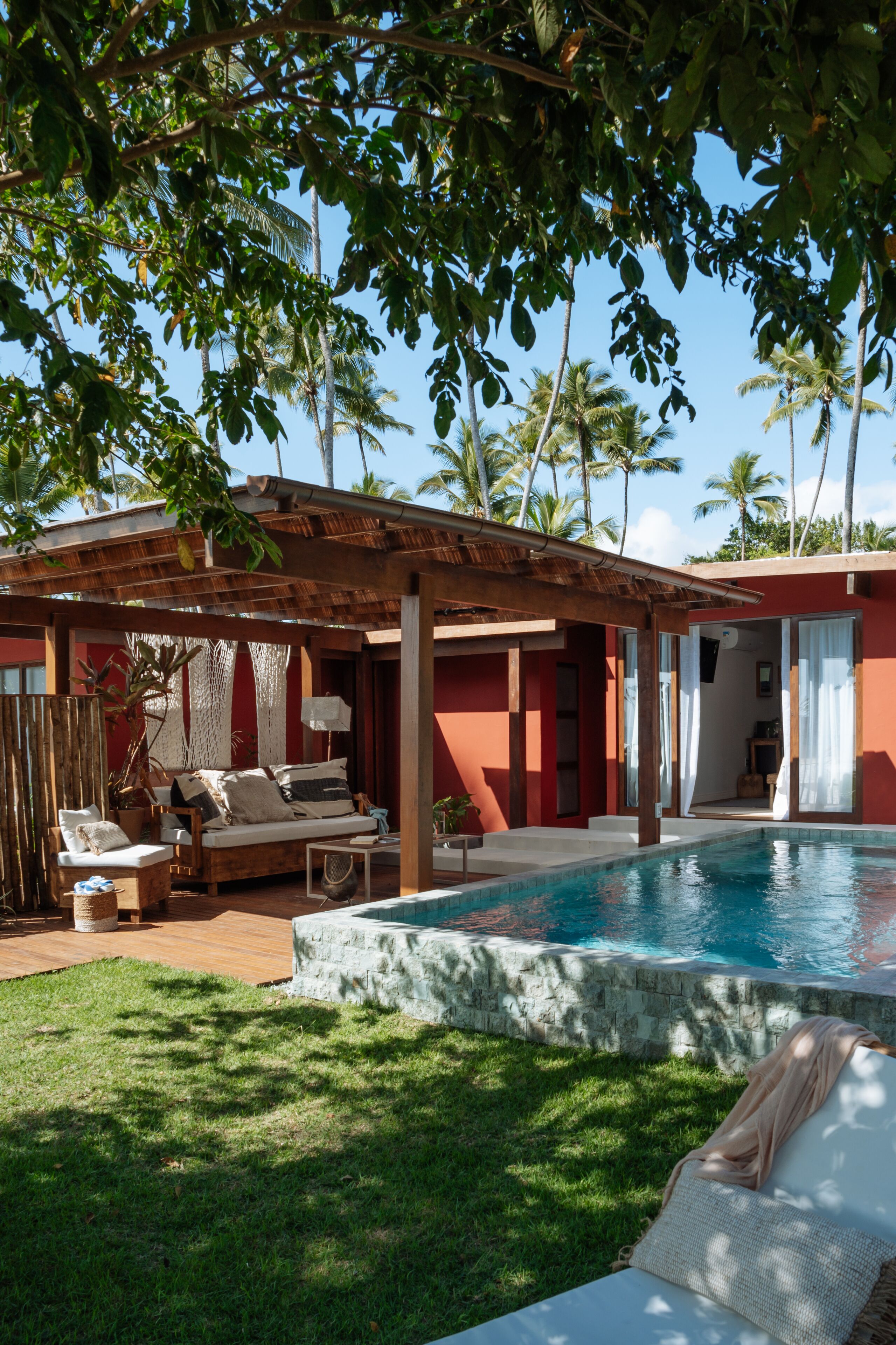 A poolside area with a wooden pergola, a sofa, and a lounge chair.
