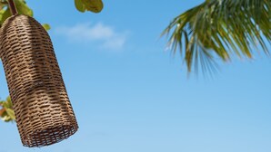 A beachside dining table with a wicker basket hanging above, a glass of water, and a plate with a fork and knife on a woven placemat. - Vila dos Orixás Boutique Hotel (Cairu)