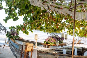 Un montaje para comer frente al mar con una mesa rústica en forma de bote, velas y centros de mesa con flores.