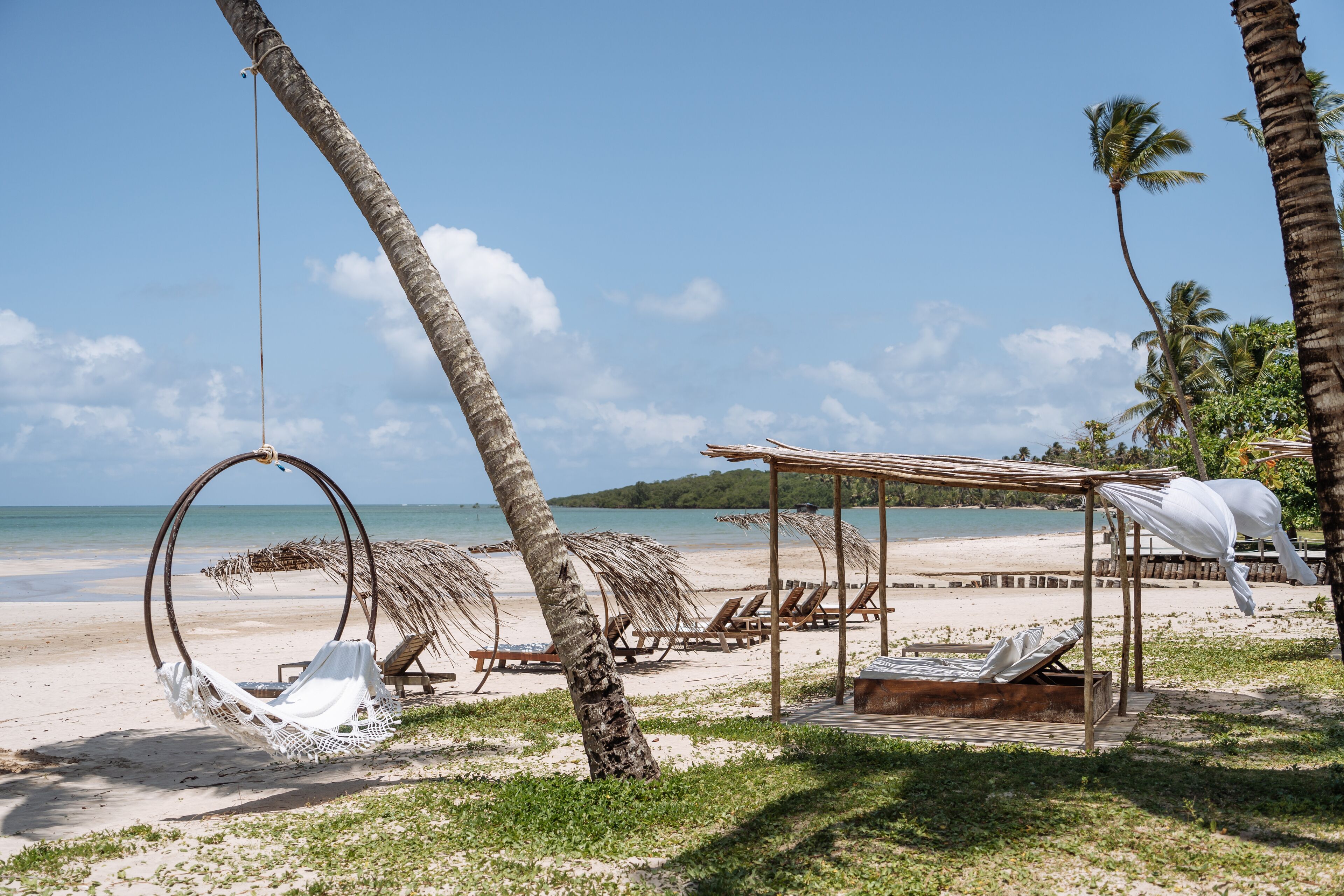 Een strand met een hangmat, ligstoelen en een houten constructie.